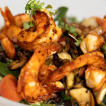 Grilled shrimp served on a bed of mixed greens, cherry tomatoes, and sautéed vegetables, garnished with fresh herbs.