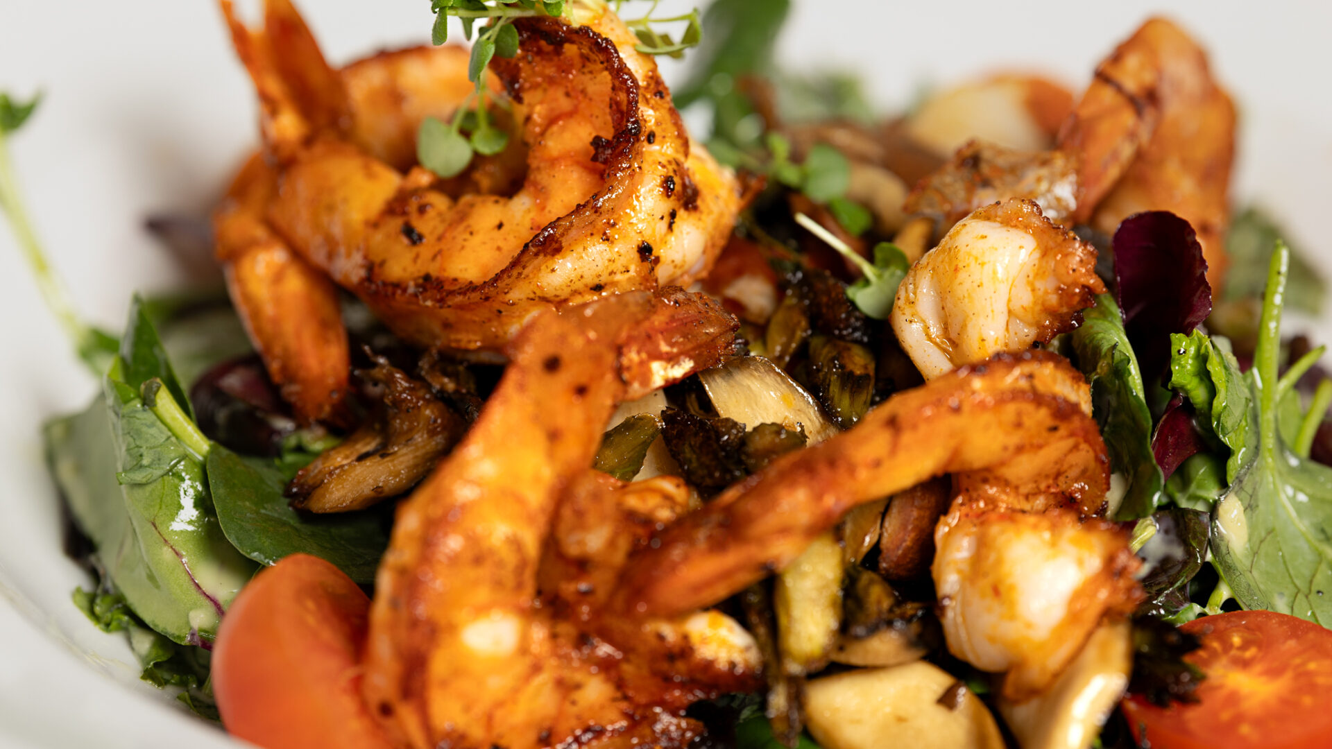 Grilled shrimp served on a bed of mixed greens, cherry tomatoes, and sautéed vegetables, garnished with fresh herbs.