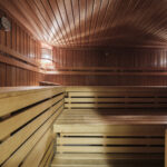 A spacious wooden sauna with tiered benches, warm lighting, and a clock on the wall, creating a relaxing and cozy atmosphere.